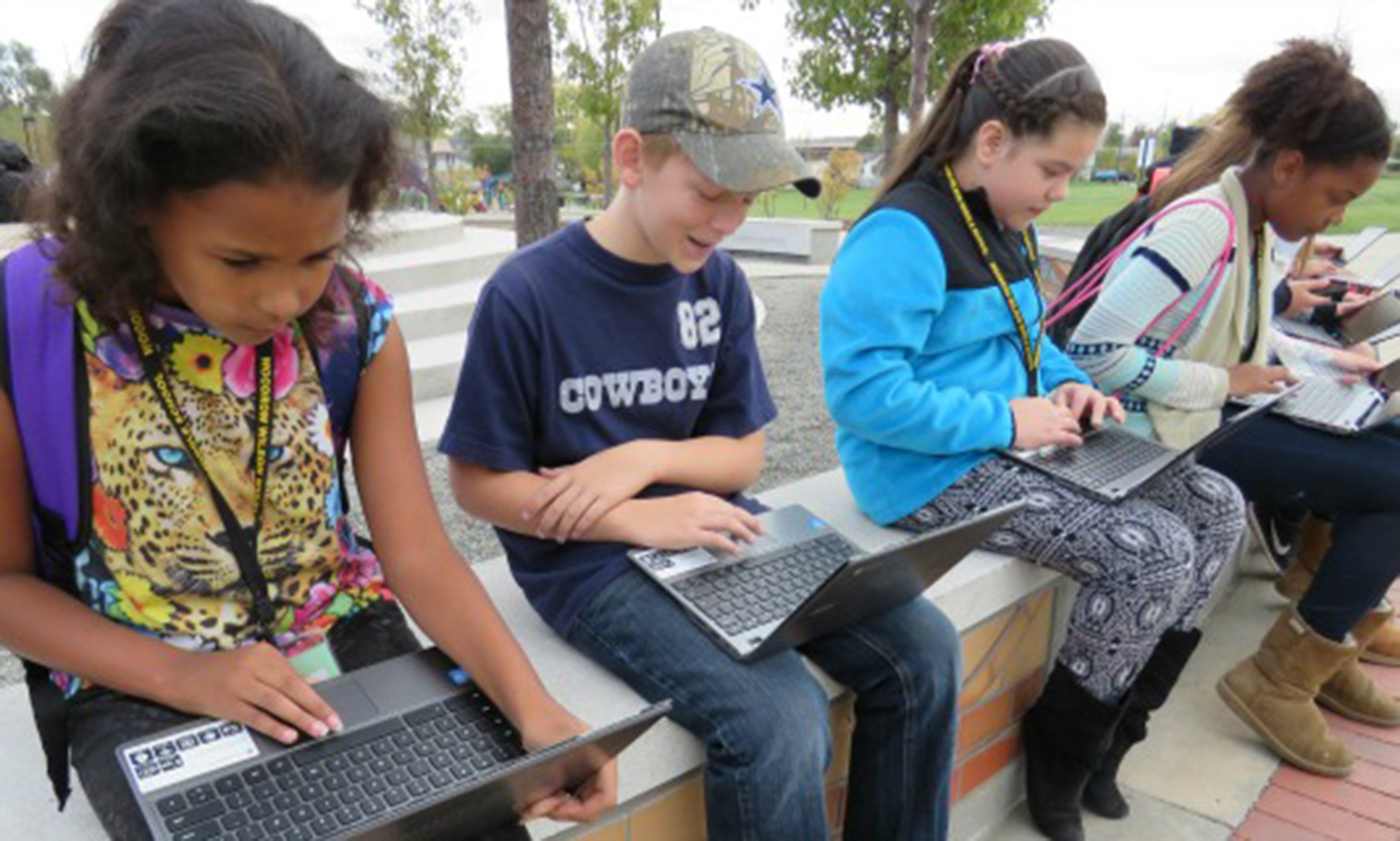 Four students, three girls and one boy, work on laptops outside