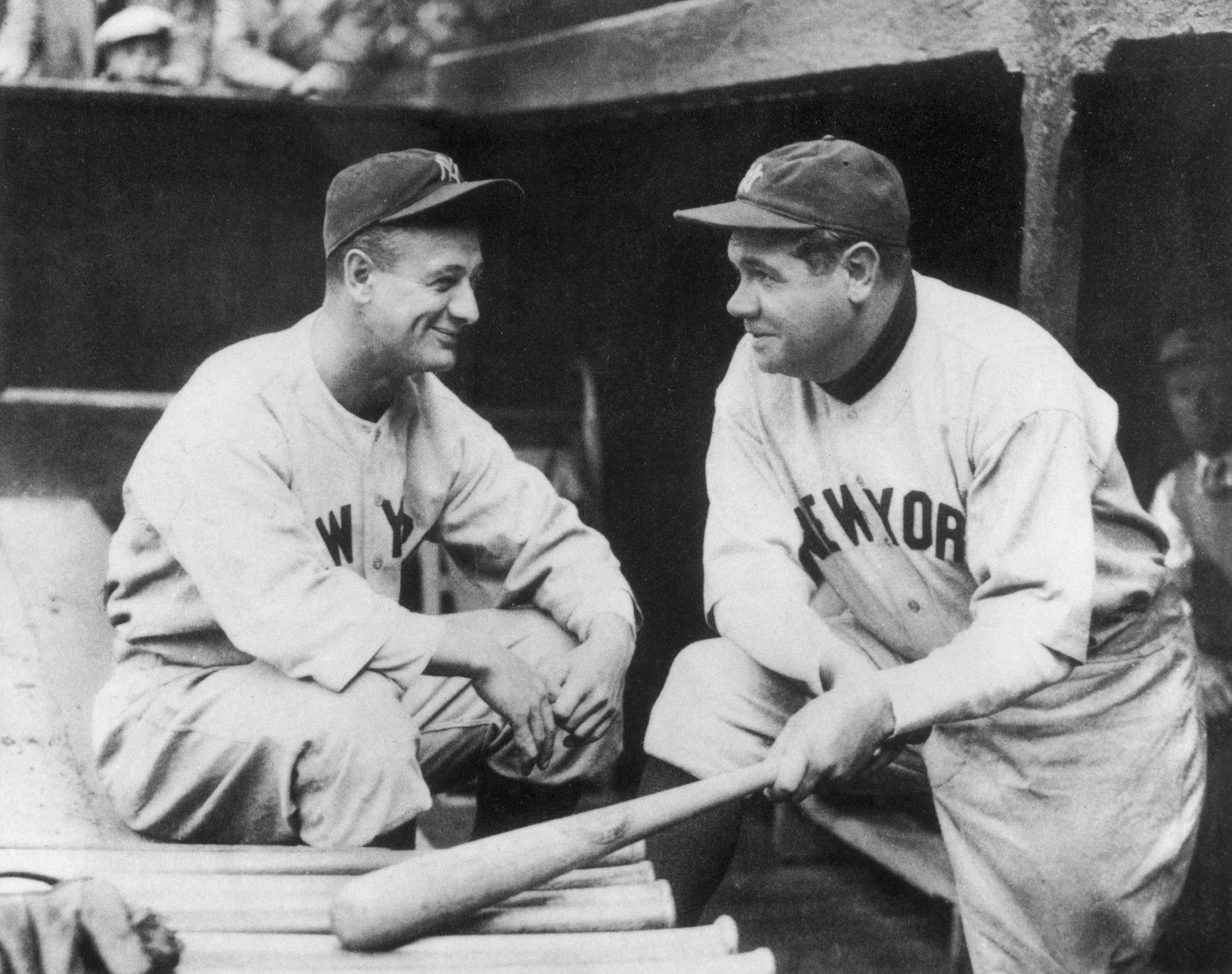 Black and white photo of Lou Gehrig, left, talking with Babe Ruth, right, in a baseball dugout