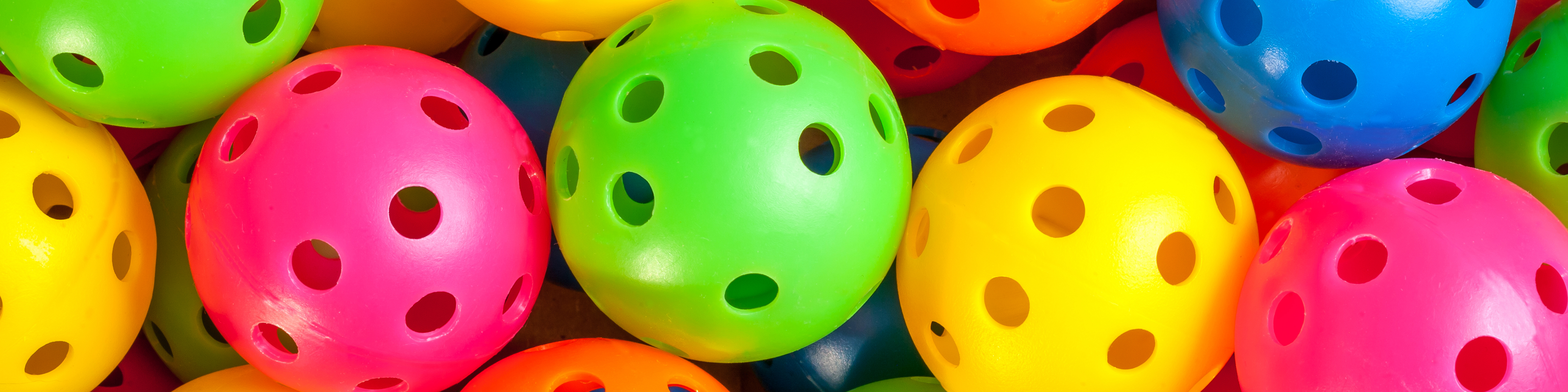 Photo of a bunch of pickleballs in blue, yellow, green, pink, and orange