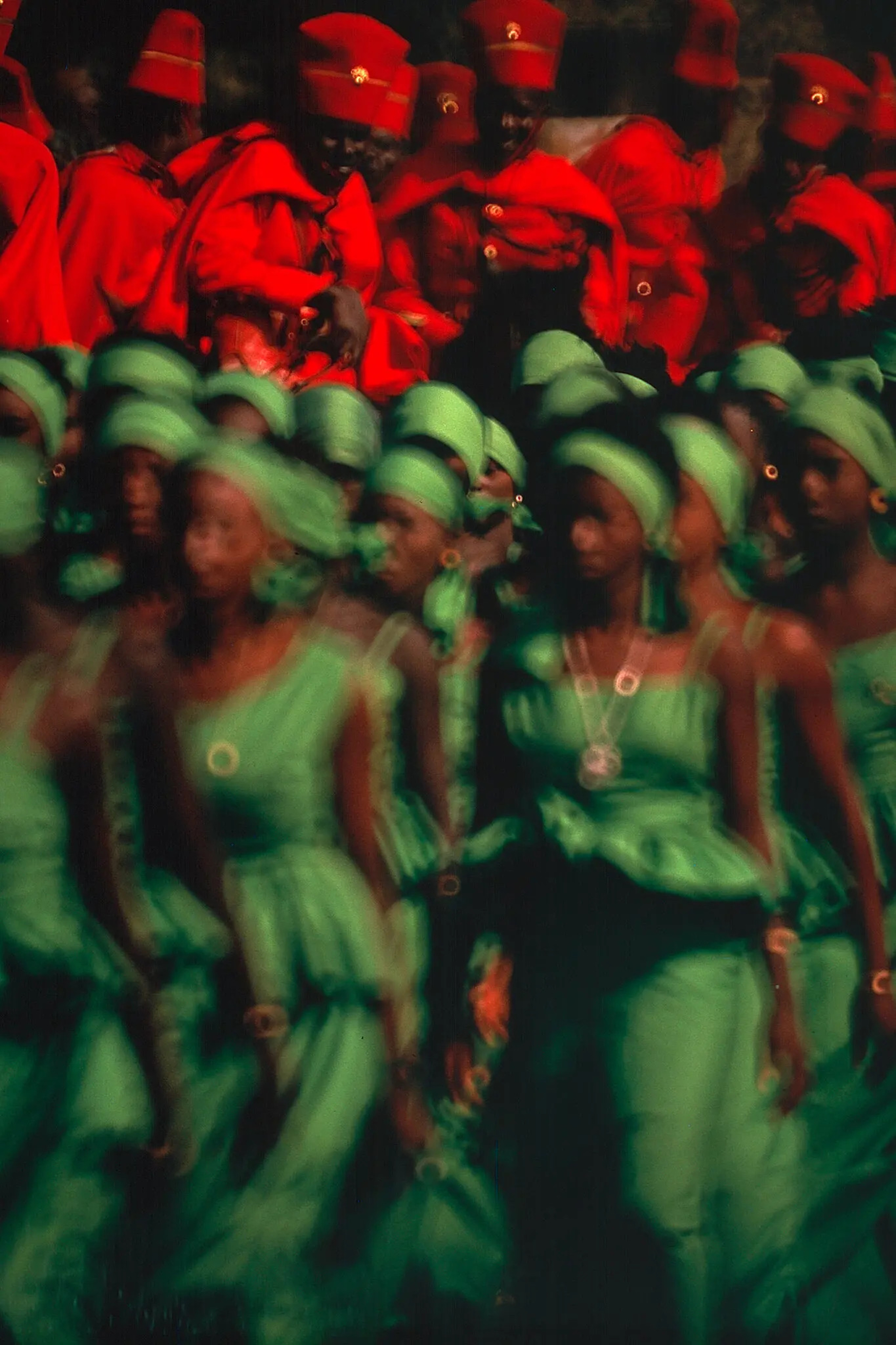 Photo of women in green dresses in the foreground and men in red uniforms in the background