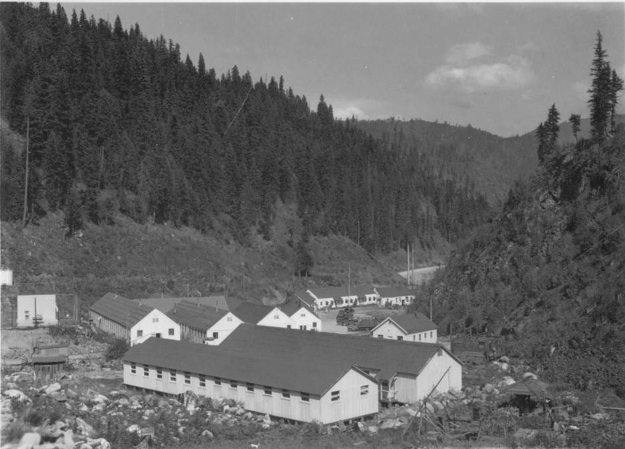 Black and white photo of single-story barracks in a wooded valley
