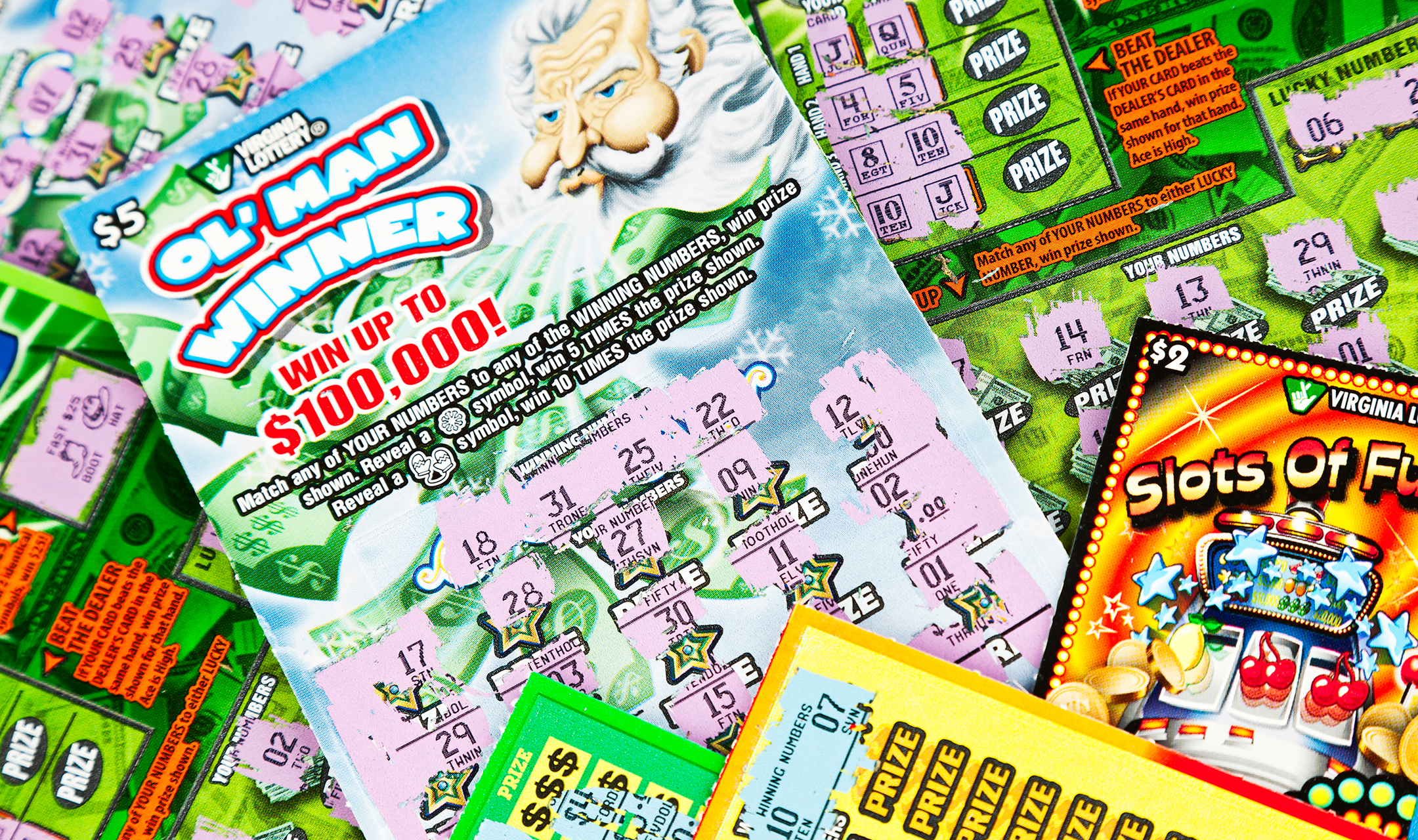 A horizontal studio shot showing an assortment of Virginia Lottery scratch-off cards that have all been scratched to reveal that each card is a losing ticket.