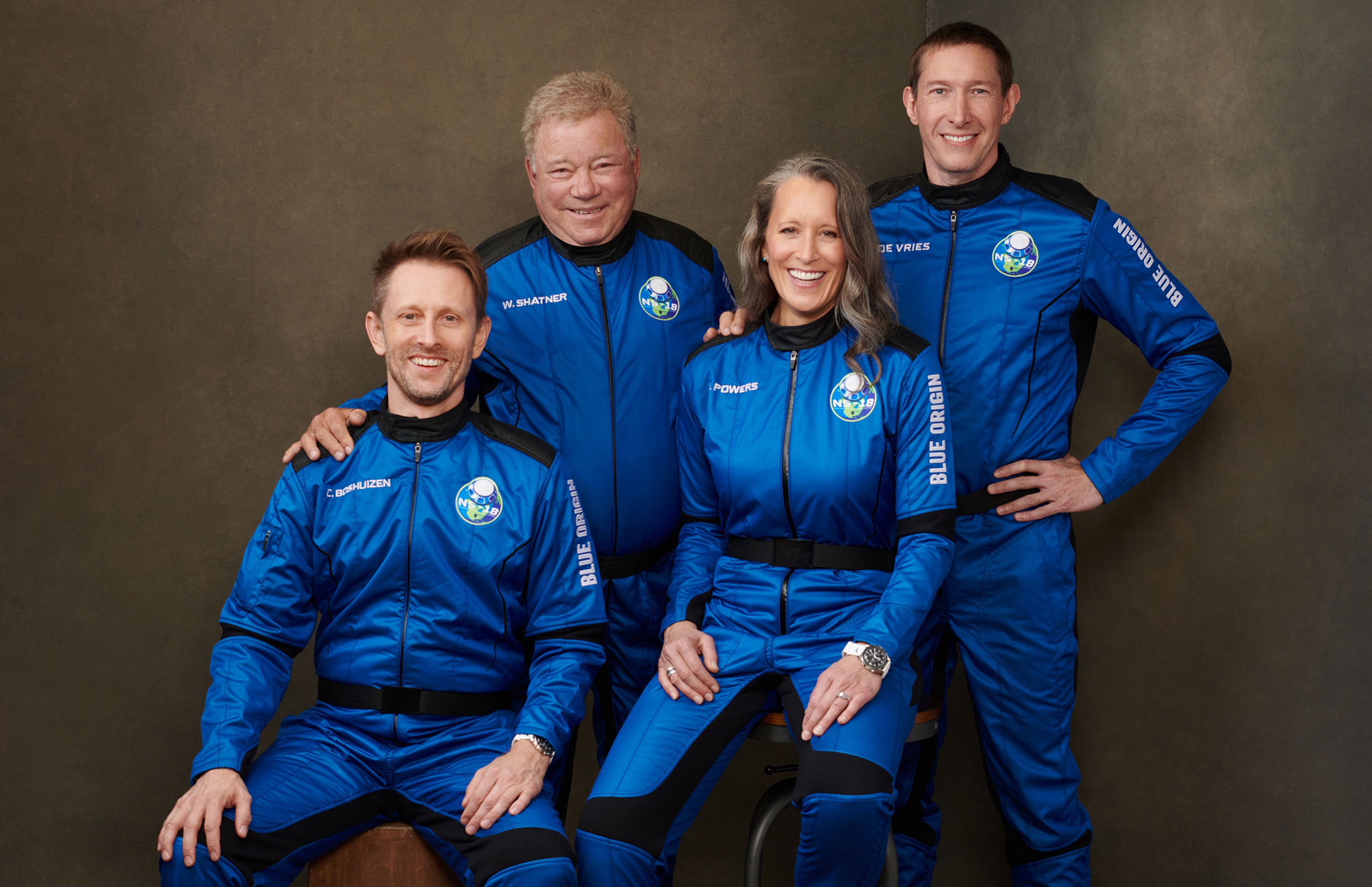 Four people in blue and black jumpsuits pose for a photograph