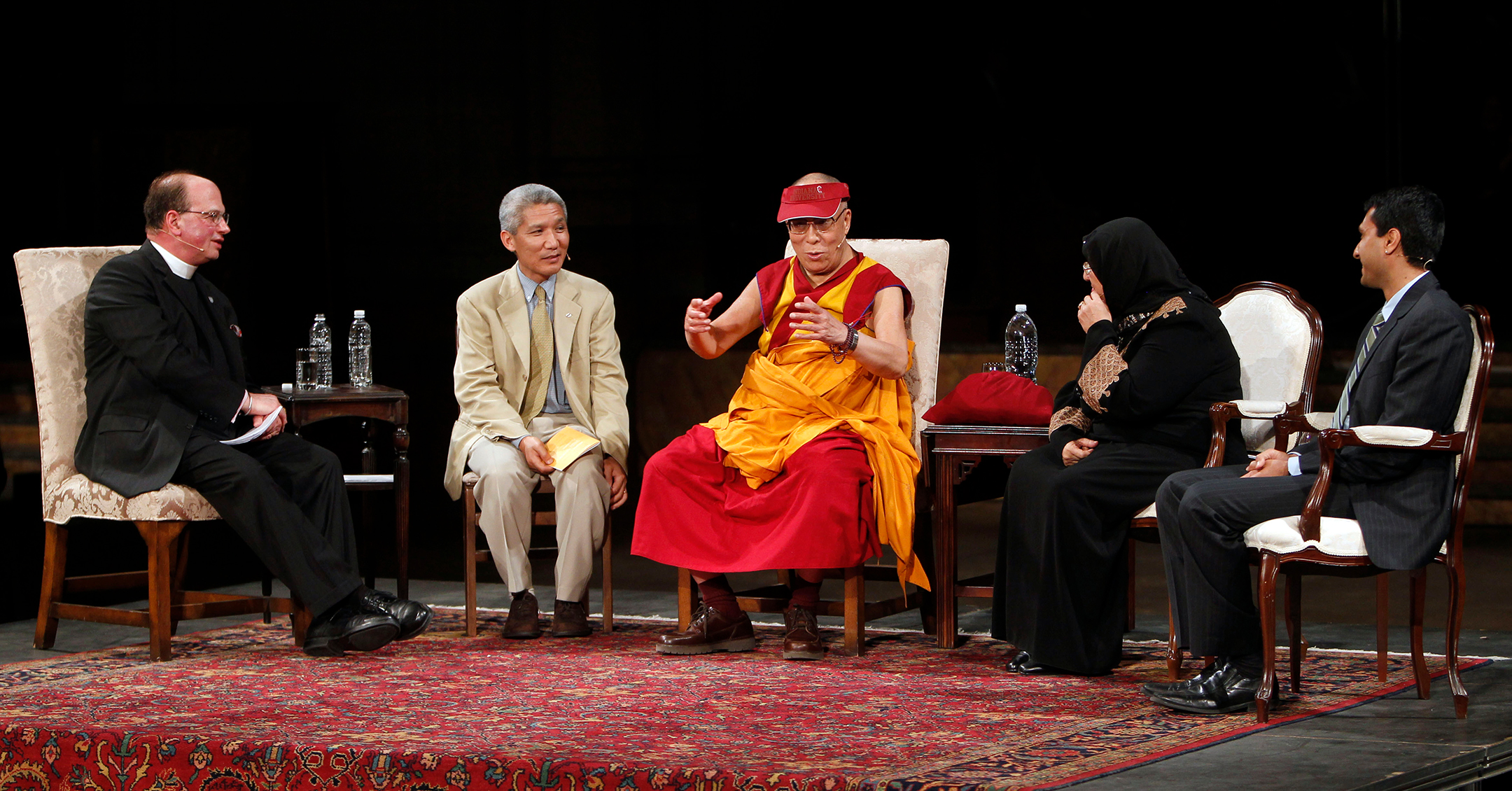 Five people sitting in chairs on a stage listening to the person in the middle who is speaking