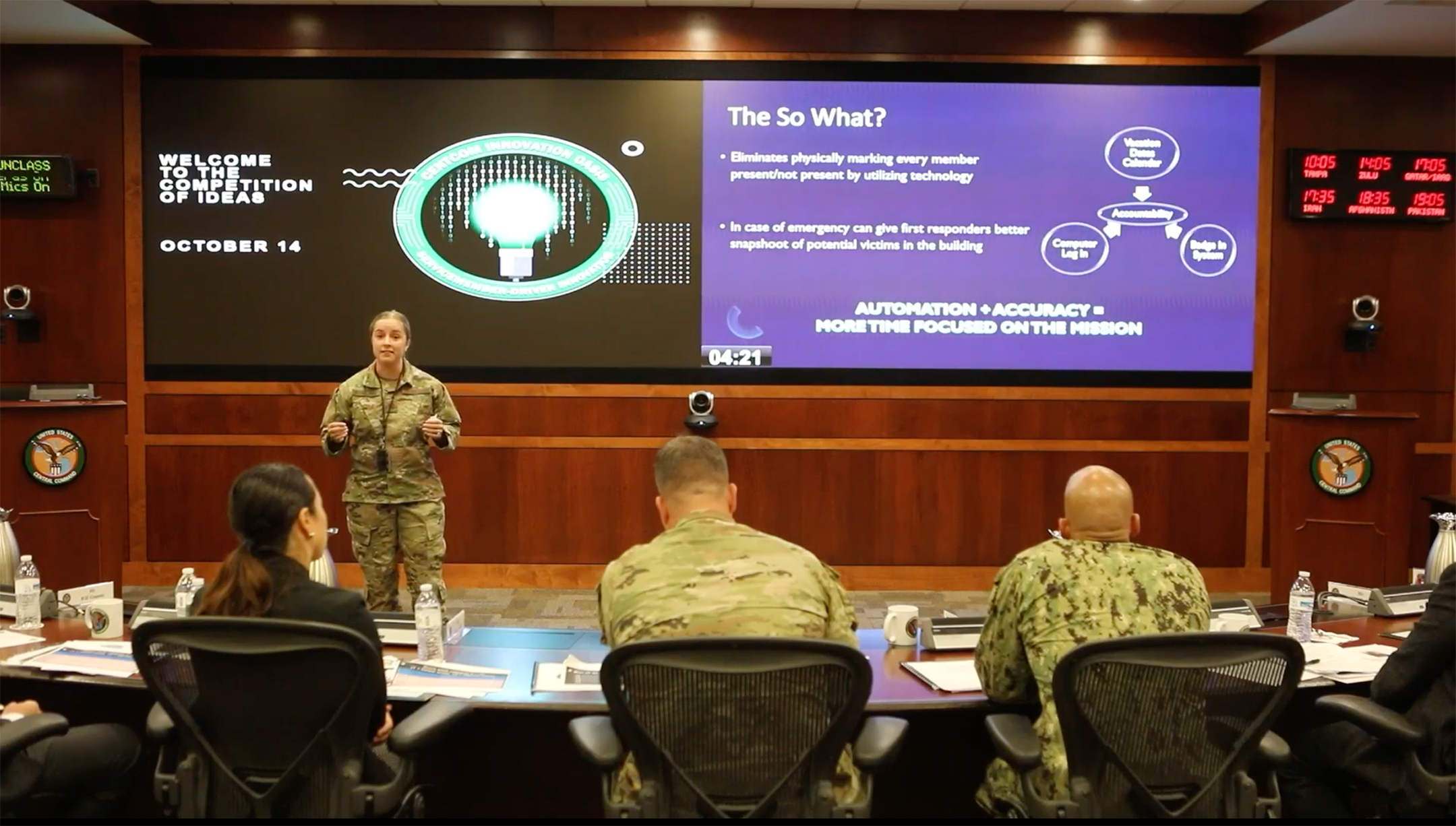 Woman in military fatigues presents to a long table of people with a screen behind her reading "Expedited Accountability"