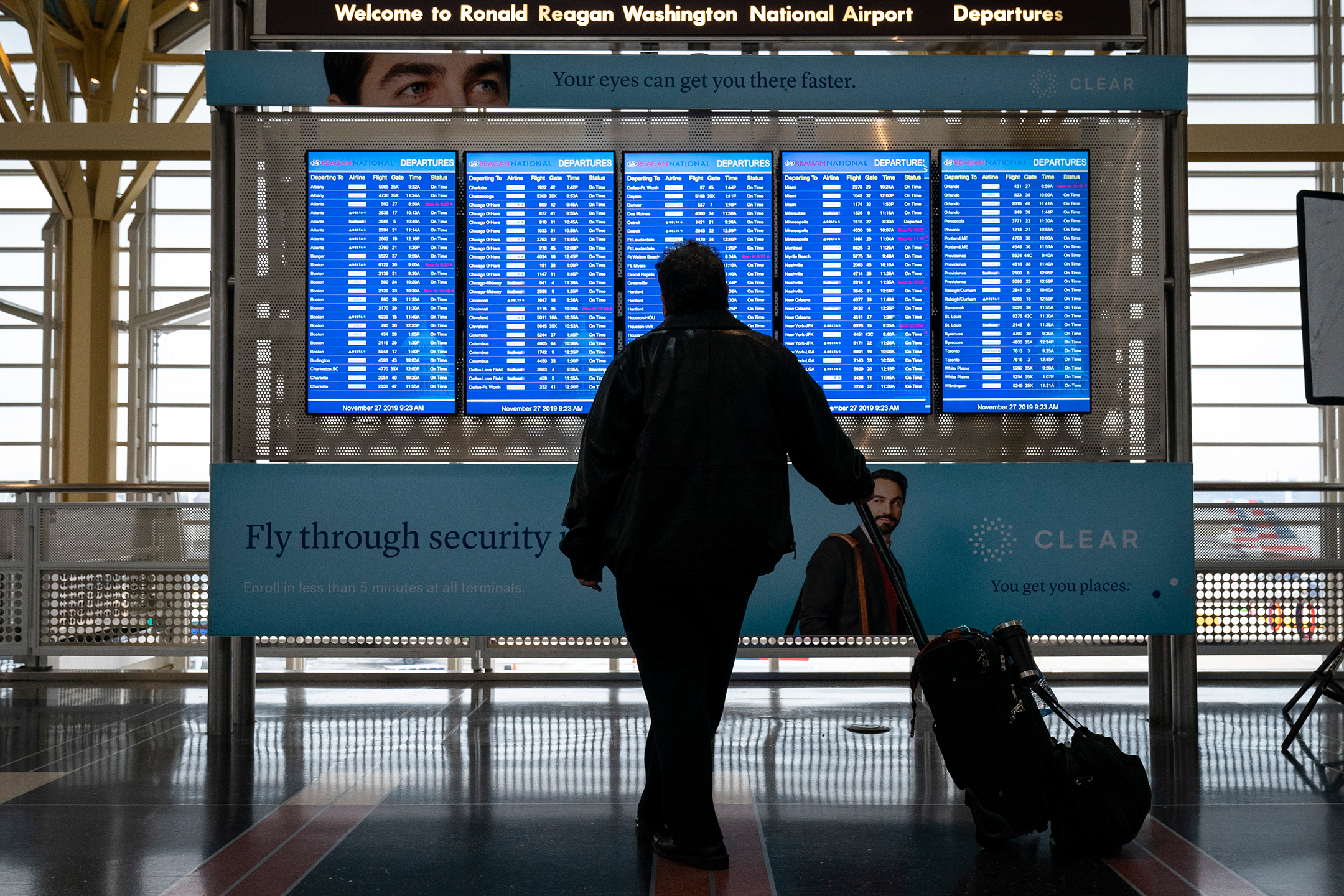 Person seen from behind looking at an airport departures bank of screens