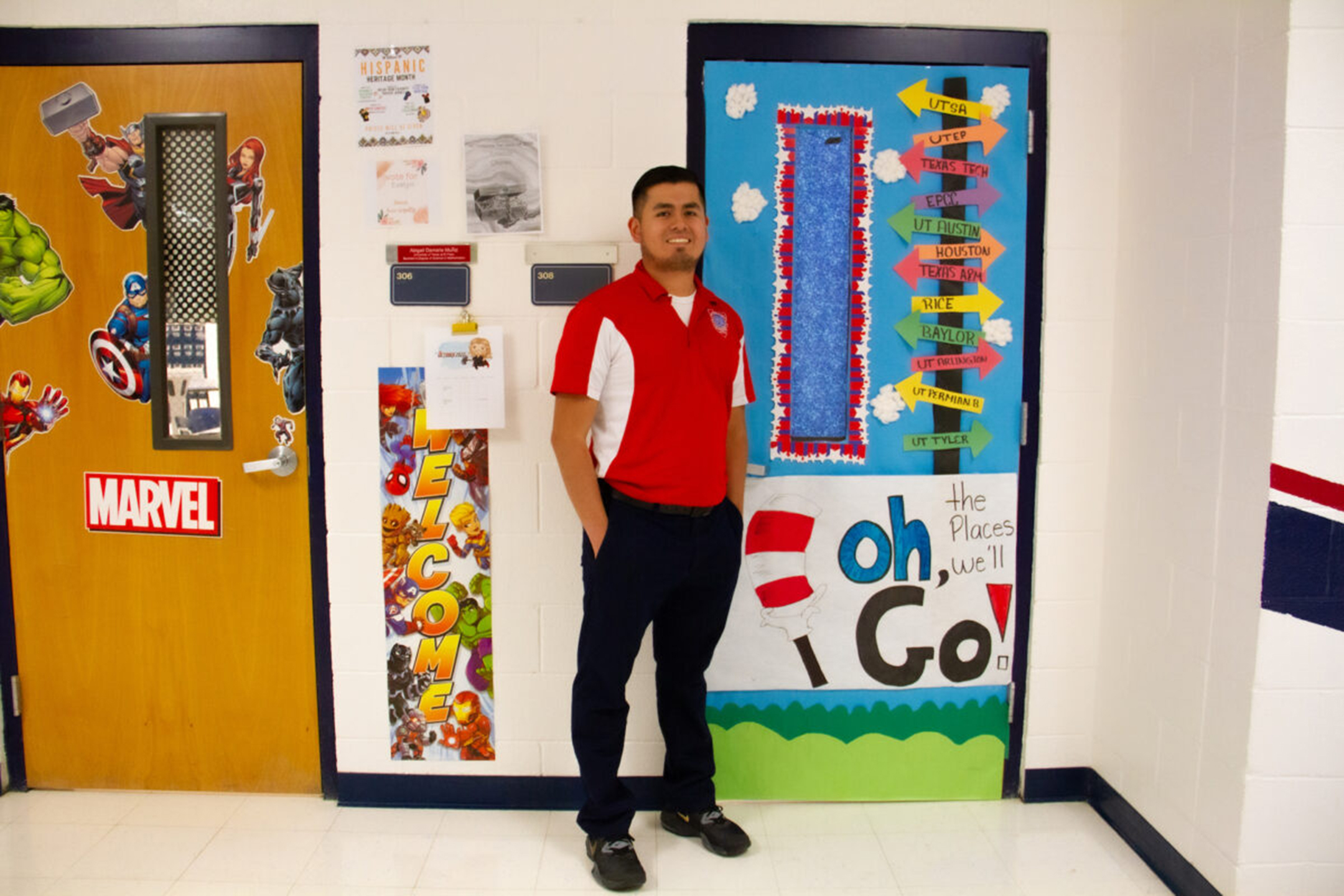 Photo of a male teacher in a red and white shirt and black pants smiling in a school hallway