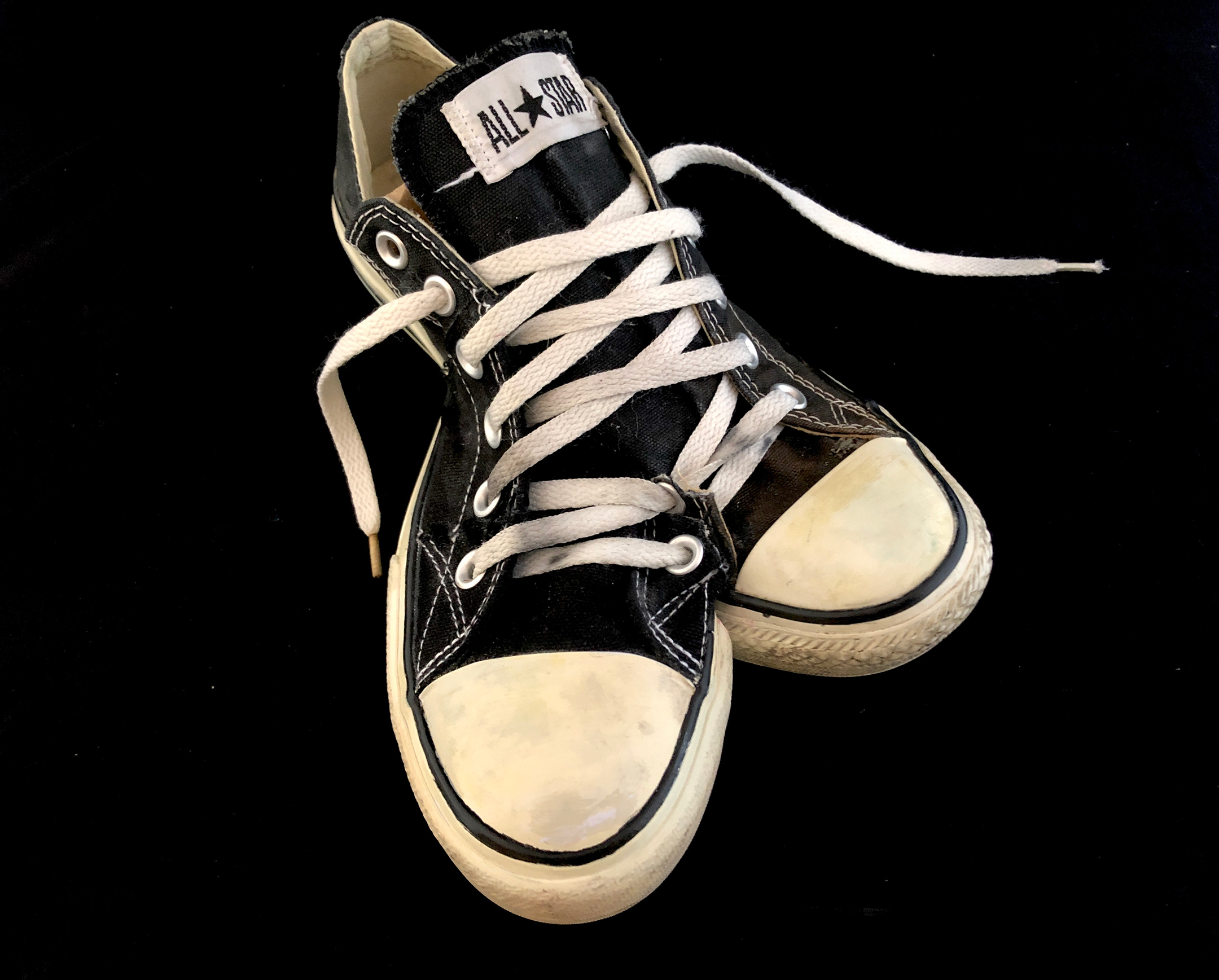 photograph of a pair of black Converse sneaker with a second black Converse sneaker stitched into it from the middle so it appears that a pair of shoes, pointing in the wrong directions, is one shoe