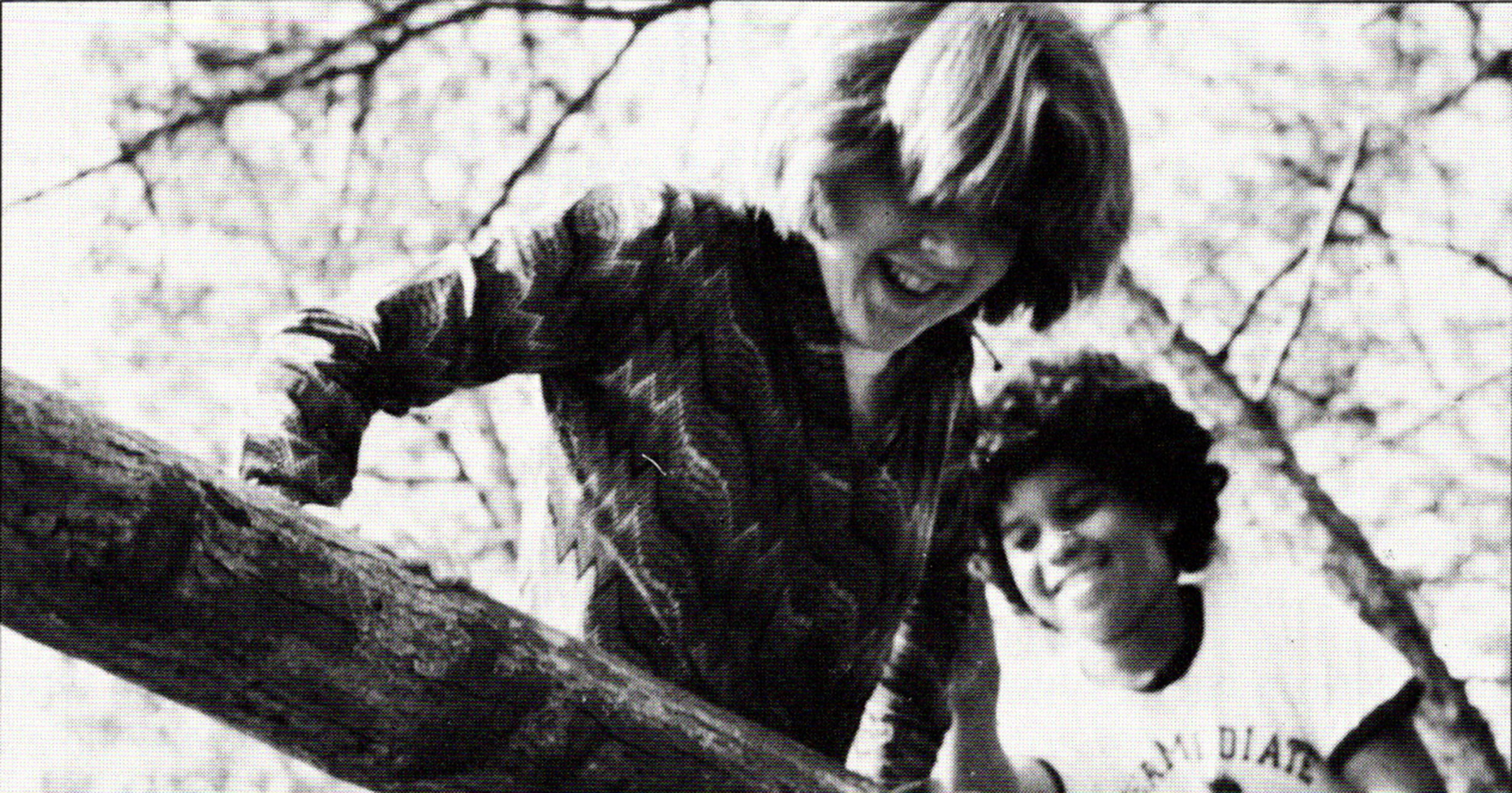 black and white photo of two students smiling as they climb over a log