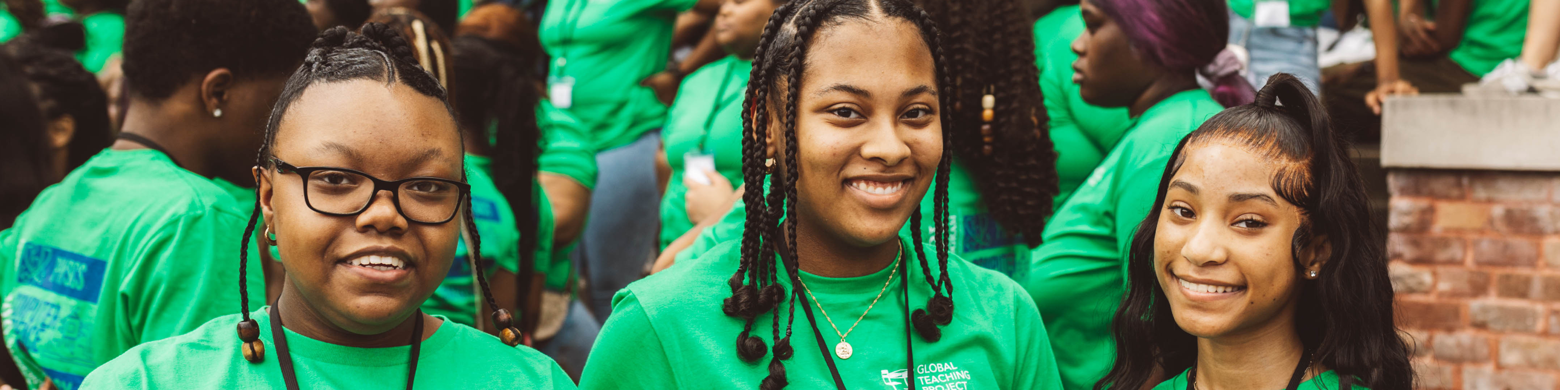 three young black women in green t-shirts smiling in a group photo