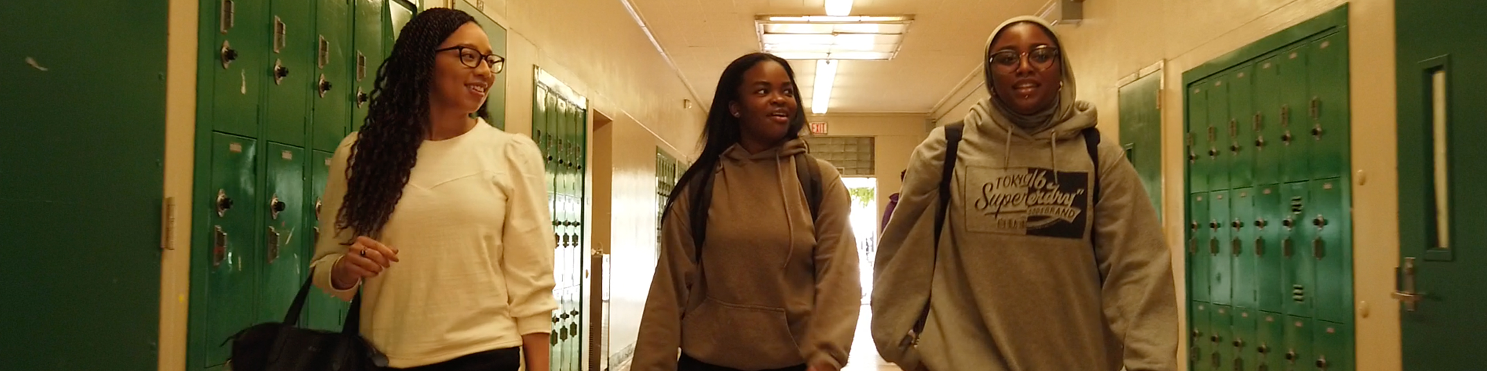 Brandi Waters, left, walks with two black female students down a high school hallway lined with green lockers