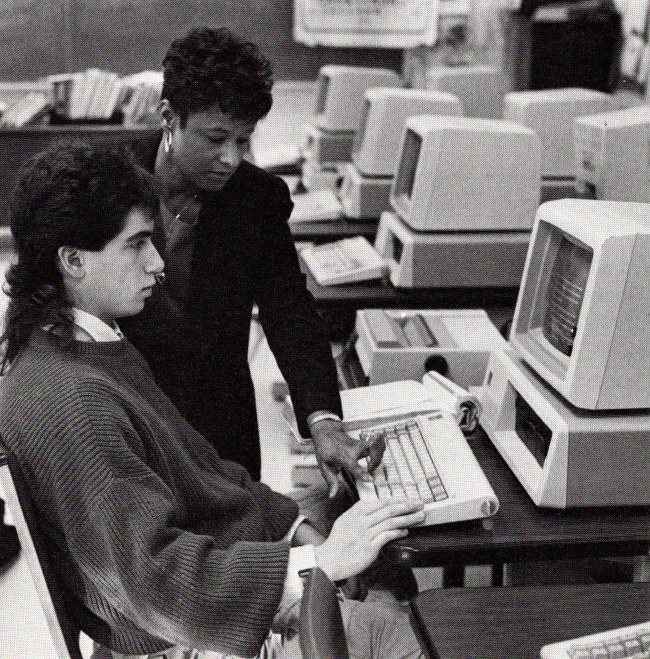 Black and white photo of a black female teacher helping a white male college student who is sitting at a computer