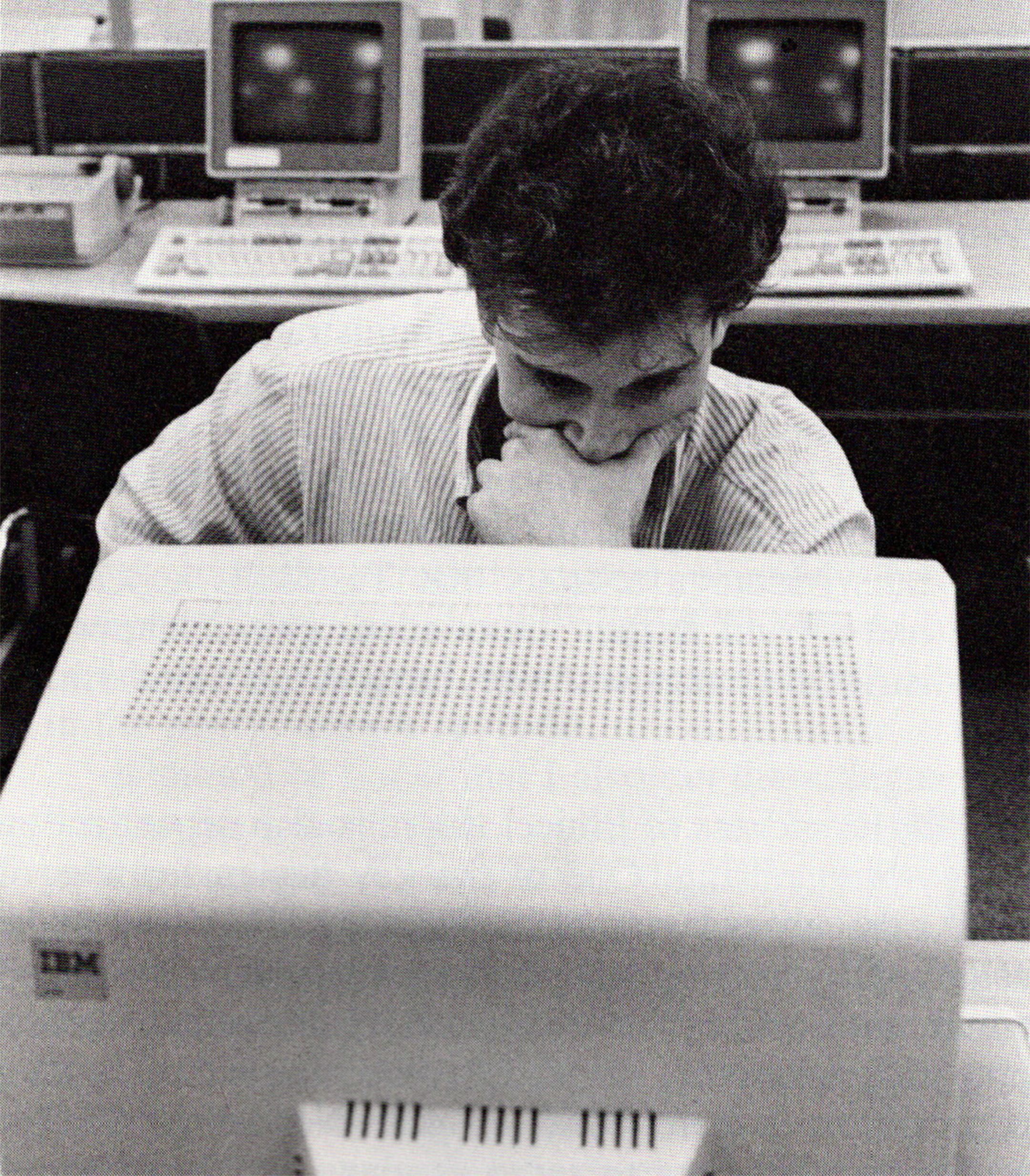Black and white photo of a male college student with his hand against his mouth and chin, looking pensively at a computer screen