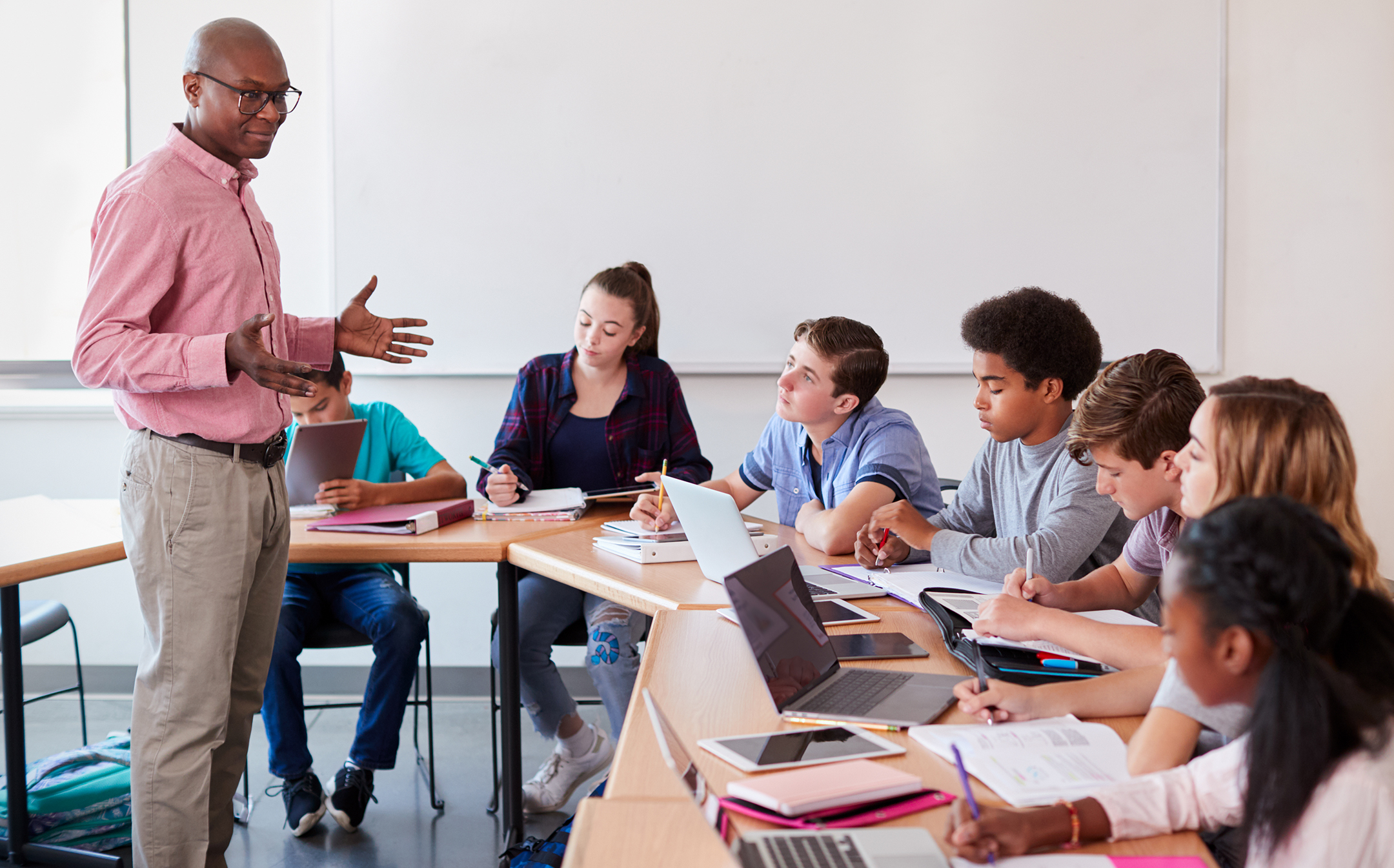 High School Teacher Talking To Pupils Using Digital Devices In Technology Class